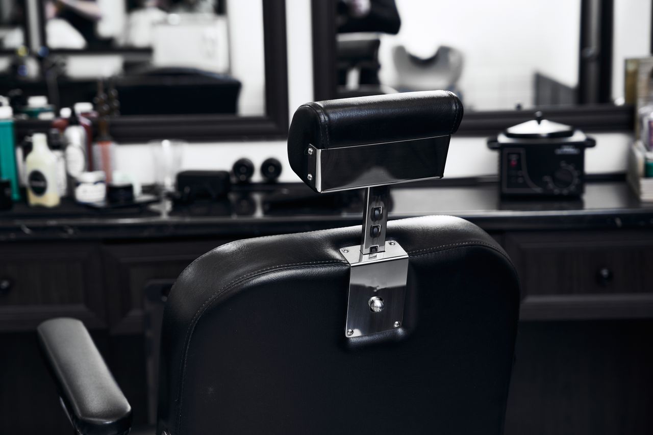 Leerer Friseurstuhl nach einem nicht wahrgenommenen Termin Leerer schwarzer Friseurstuhl vor einem Spiegel in einem Friseursalon