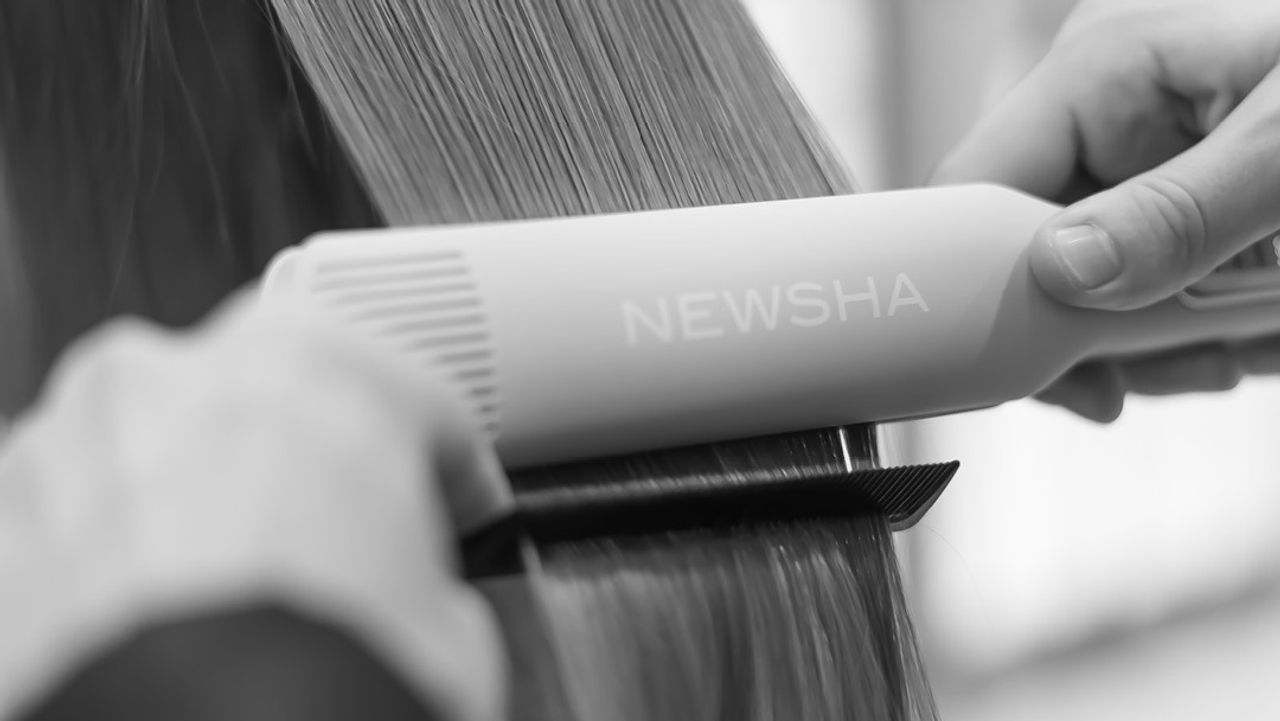Friseurin glättet langes Haar mit einem NEWSHA-Glätteisen und Kamm