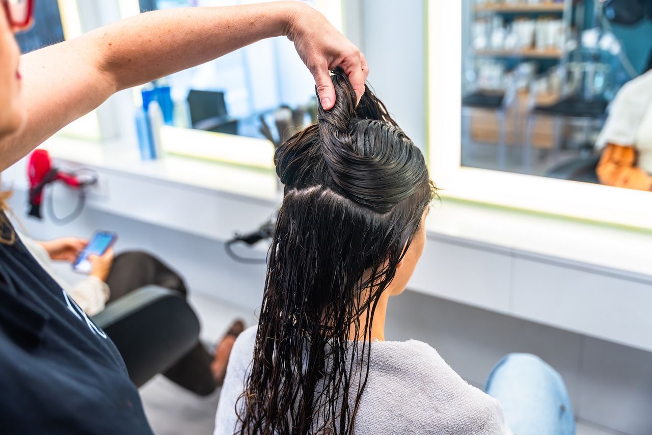 Friseurin teilt das nasse, handtuchtrockene Haar einer Kundin ab, um die Haarbotox-Behandlung Strähne für Strähne aufzutragen