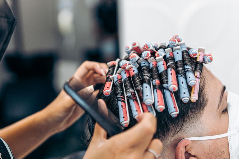 Nahaufnahme eines Friseurs, der die Haare eines Mannes mit Dauerwellwicklern aufwickelt